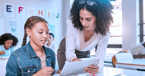 A female teacher teaching a female student on a tablet.