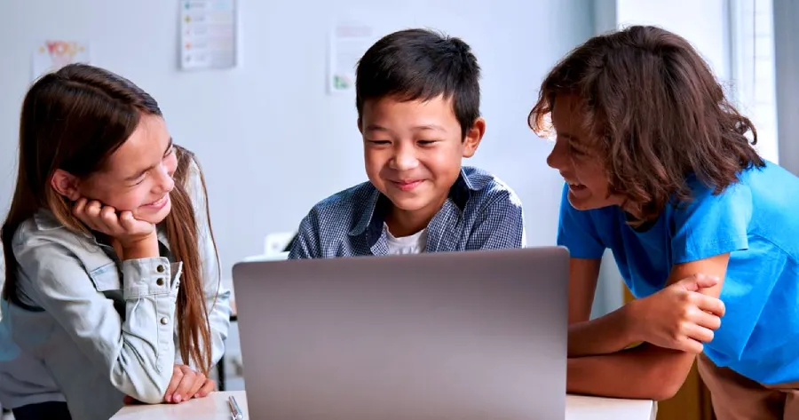3 students looking at a laptop screen and smiling. 