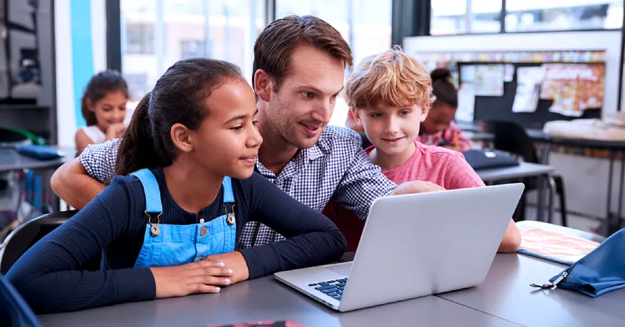 2 students, a boy, and a girl are sitting with a teacher as they look at a laptop screen. 