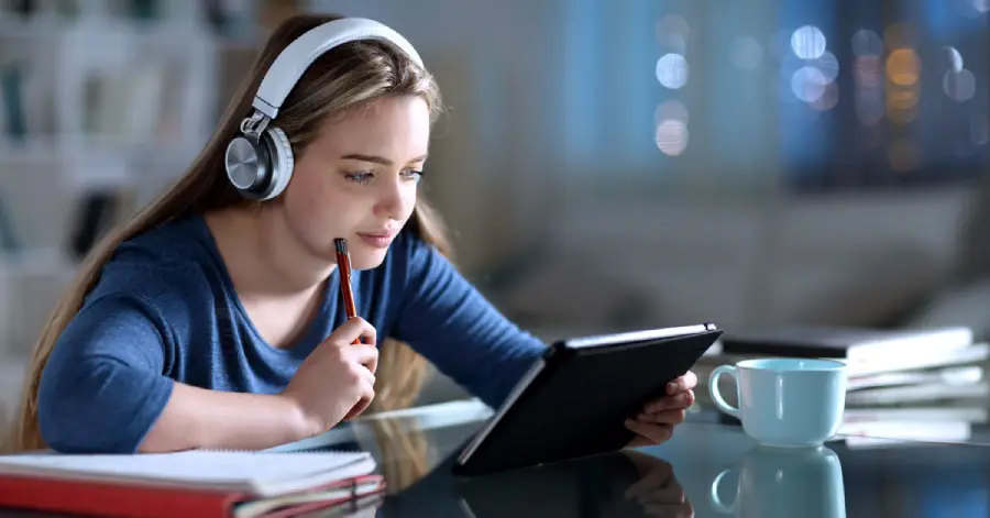  A girl student wearing headphones is watching a digital storytelling in education video on a tablet. 