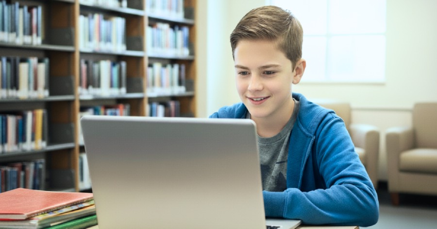 A student working on a laptop in a library, learning about the AI literacy programs in K-12 education. 