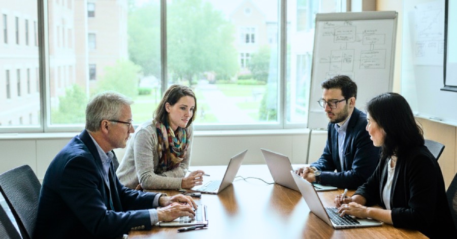 A group of university leaders sitting together in a conference room with their laptops, discussing strategies for implementing DataOps for university leaders to enhance decision-making and compliance. 