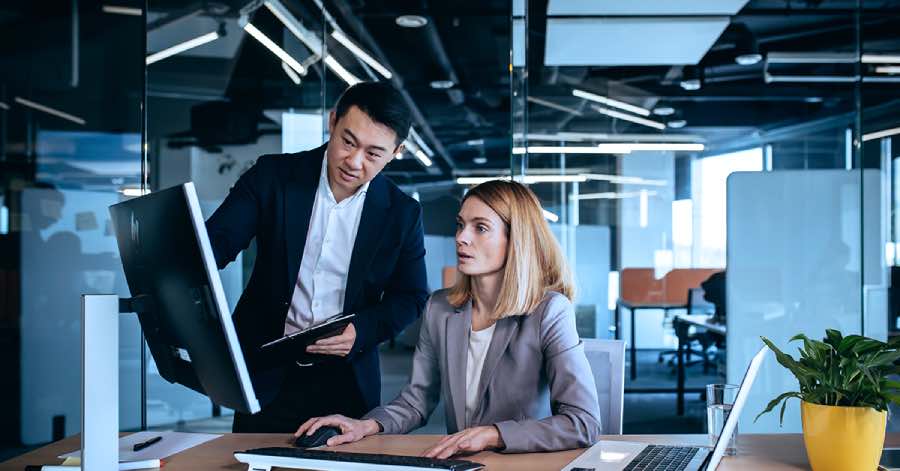 Two professionals in an office setting reviewing performance data on a desktop screen, collaborating on AI tutor benchmarking analysis to evaluate system accuracy and learning outcomes.