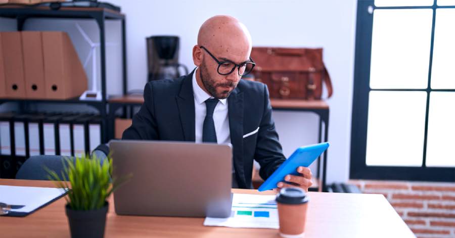 A legal professional in a suit reviewing documents on a tablet while working at a desk with a laptop, showcasing AI VPAT compliance automation for assessing digital accessibility and generating compliance reports.