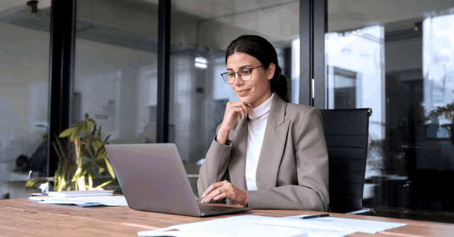 A woman in an office setting working on a laptop, representing strategic planning and implementation of data governance for K-12 districts.