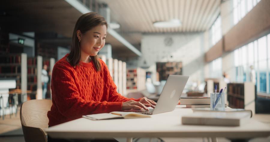 A learner in a university accessing the content gone through the higher education simulation vendor evaluation on a laptop while studying at a university library desk.