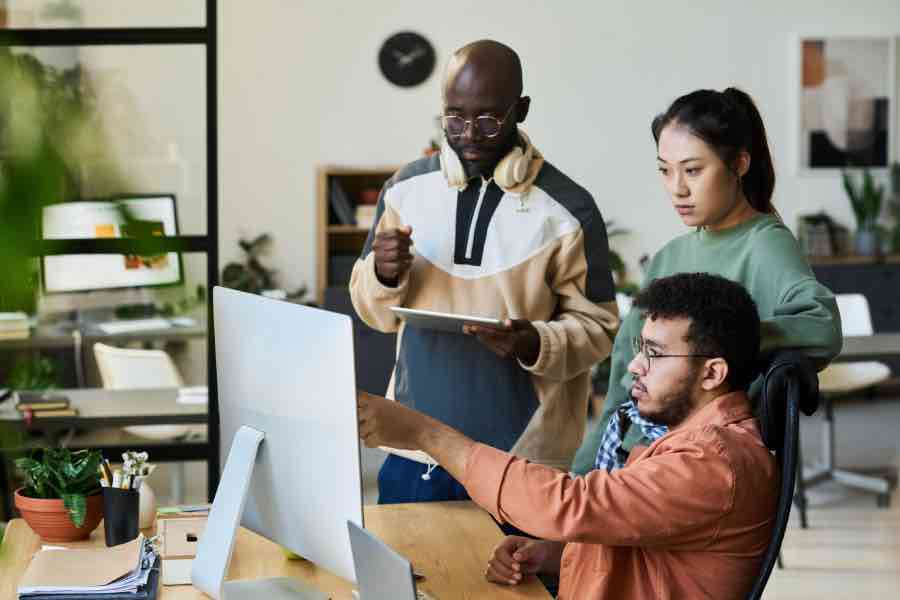 A diverse group of individuals working together in a modern office environment, creating content on a computer and tablet device, and discussing how it can be improved, representing the concept of learning media design for effective learning.