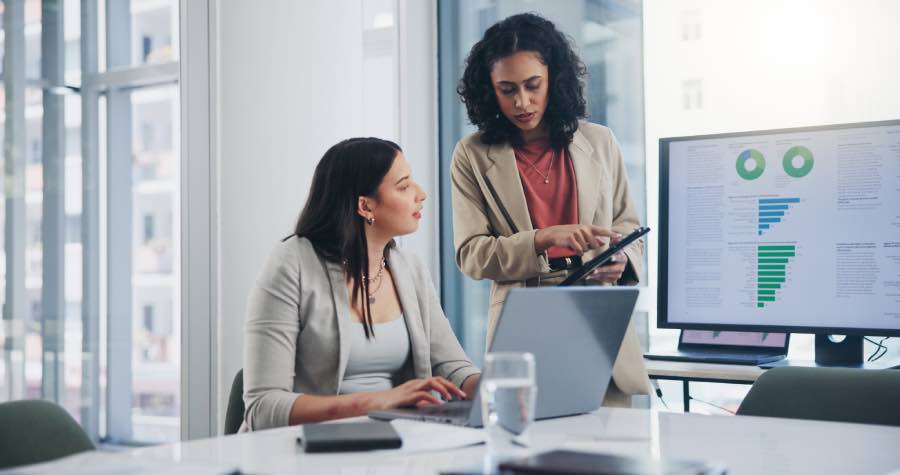 Two professionals reviewing charts on a monitor and tablet in a modern office, analyzing multimodal tutoring data to guide AI-driven learning insights