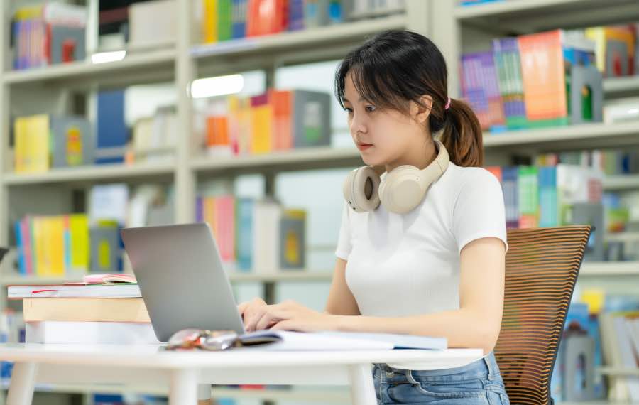 A college student working independently on a laptop in a library, reflecting how student agency in higher education retention is supported through self-directed learning and focused study environments.