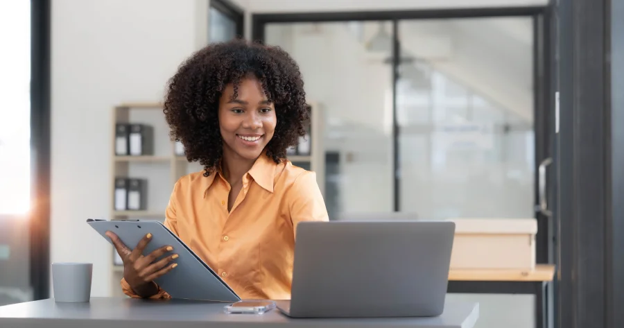 A working professional at a desk with a laptop and tablet in a modern office, reviewing digital content and workflows as part of an accessibility audit at scale to support inclusive and compliant user experiences.