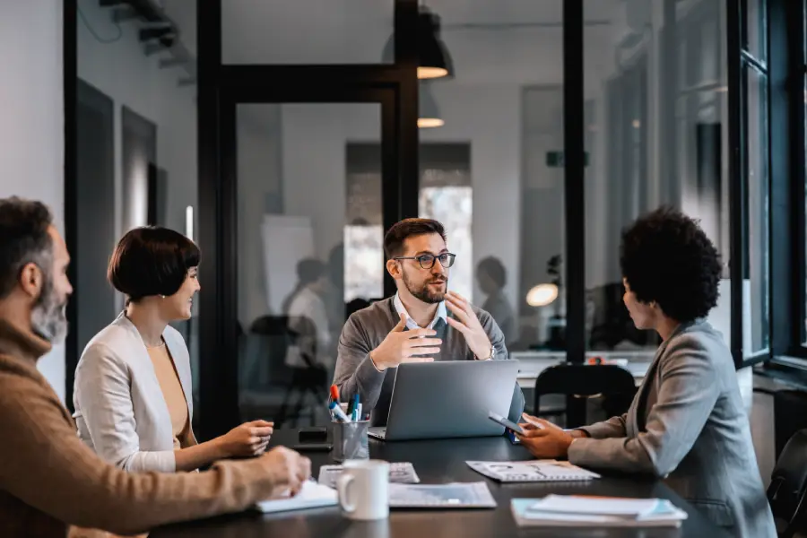 A group of working professionals around a conference table during a strategic planning meeting, discussing policies, risk management, and governance frameworks aligned with Generative AI Product Safety Standards for responsible technology deployment in educational organisations.