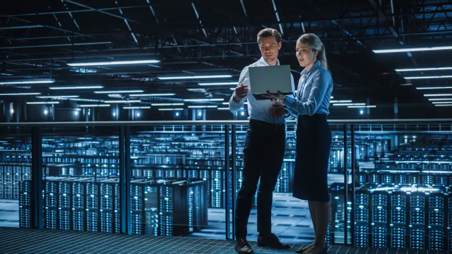Two IT professionals reviewing infrastructure and server performance in a large data center as part of Moodle upgrade planning, assessing system readiness, capacity, and maintenance requirements before a platform upgrade.