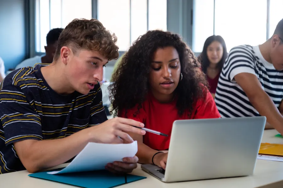 College students collaborate on a laptop during a classroom session, learning from the documents and digital coursework that support ADA Title II compliance.