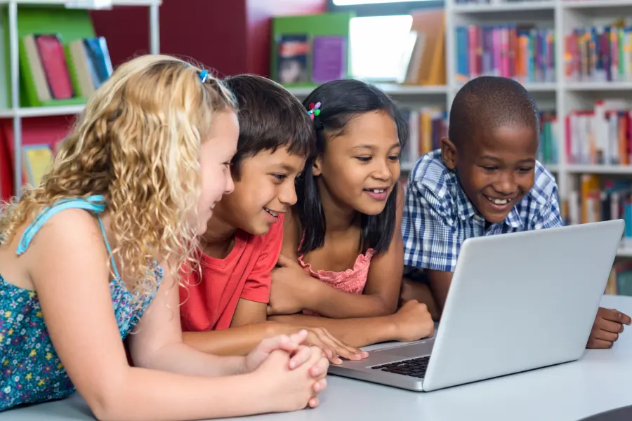 Four elementary school students gathered around a laptop in a school library, highlighting the importance of K-12 accessibility audits for creating inclusive digital learning experiences.